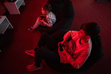 İki erkek oyuncu kırmızı oyun odasında oyun konsolu oynuyorlar..