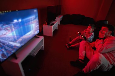 Baba ve oğlu kırmızı oyun odasında oyun konsolu oynuyorlar. Baba ve çocuk oyuncular.