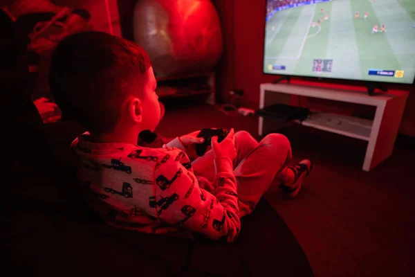 Boy gamer play gamepad football video game console in red gaming room.
