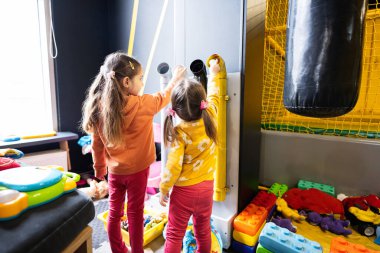 Two sisters throw balls inside tubes at kids play center. clipart