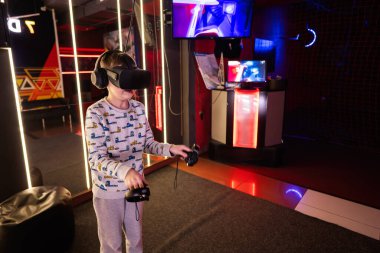 Çocuk oyun oynarken sanal gerçeklik kulaklığı ve oyun konsolu kullanıyor..