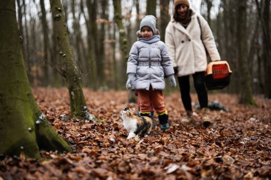 Mother and daughters walking with cat travel plastic cage carriage outdoor at wood.