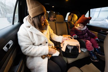 Mother and daughters with cat travel plastic cage carriage in car. 