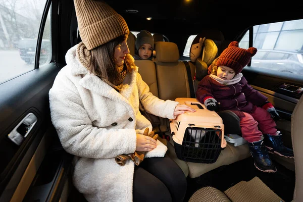 Mother and daughters with cat travel plastic cage carriage in car.