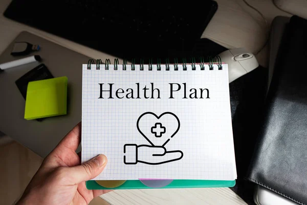 Health plan word on notebook holding man against desktop.