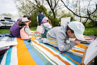 Mutlu genç aile, anne ve çocuklar bahçedeki bahar parkında piknik battaniyesinde eğleniyor ve eğleniyorlar..