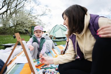 Mutlu genç aile, anne ve çocuklar bahçedeki bahar parkında piknik battaniyesinde eğleniyor ve eğleniyorlar..