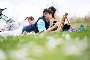 Mutlu genç aile, anne ve çocuklar bahçedeki bahar parkında piknik battaniyesinde eğleniyor ve eğleniyorlar..
