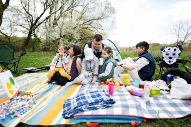 Bahçedeki bahar parkında piknik battaniyesinde eğlenen ve eğlenen dört çocuklu mutlu bir aile..