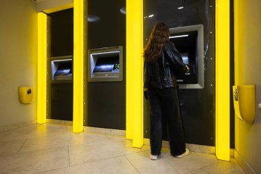 Genç esmer kız sarı ATM 'de kredi kartından para çekiyor..