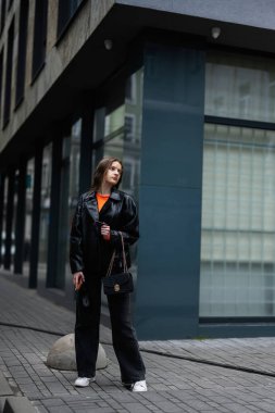 Deri ceketli genç bayan elinde kredi kartıyla şehir merkezinde duruyor..