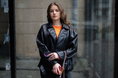 Deri ceketli genç bayan elinde kredi kartıyla şehir merkezinde duruyor..