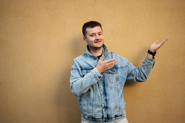 Portrait of stylish man in jeans jacket against yellow wall hand gesture at copy space.