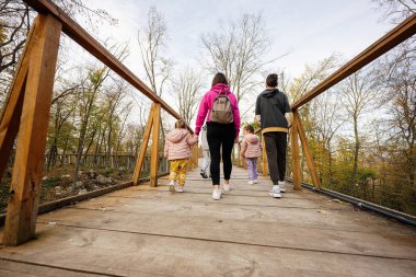 Annelerinin sırtında dört çocukla sonbahar ormanlarında ahşap köprüde yürüyorlar..