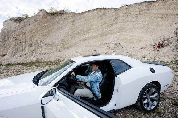 Przystojny Mężczyzna Jeansowej Kurtce Czepku Siedzi Przy Swoim Białym Samochodzie — Zdjęcie stockowe