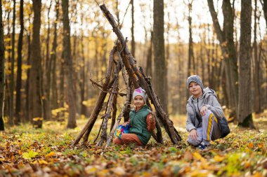 Erkek ve kız kardeşi sonbahar ormanında ağaçlardan bir ev inşa ediyor..