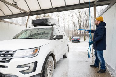 Man washing american SUV car with roof rack at a self service wash in cold weather.