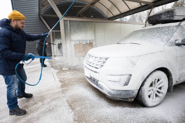 Man washing american SUV car with roof rack at a self service wash in cold weather.