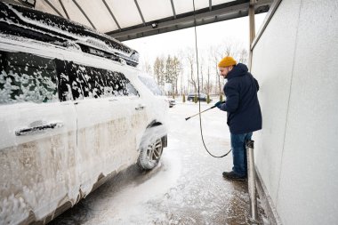 Man washing high pressure water american SUV car with roof rack at self service wash in cold weather.