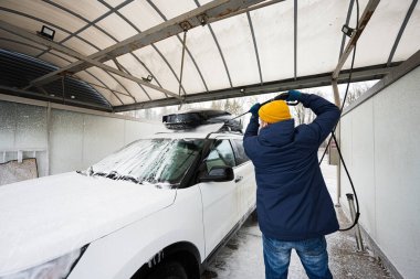 Man washing high pressure water american SUV car with roof rack at self service wash in cold weather.