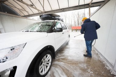 Man washing high pressure water american SUV car with roof rack at self service wash in cold weather.