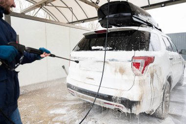 Man washing high pressure water american SUV car with roof rack at self service wash in cold weather.