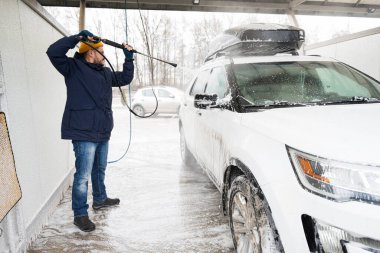 Man washing high pressure water american SUV car with roof rack at self service wash in cold weather.