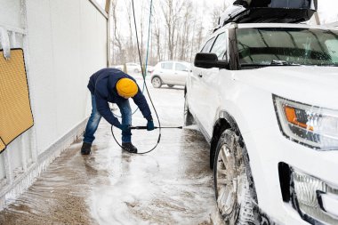 Man washing high pressure water american SUV car with roof rack at self service wash in cold weather.