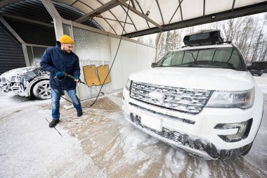 Man washing high pressure water american SUV car with roof rack at self service wash in cold weather.
