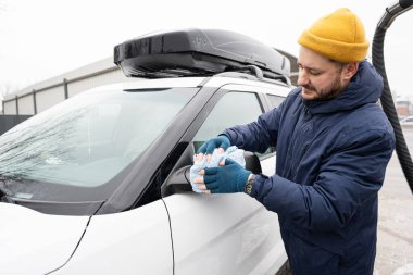 Man wipes american SUV car mirror with a microfiber cloth after washing in cold weather.