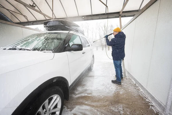 stock image Man washing high pressure water american SUV car with roof rack at self service wash in cold weather.