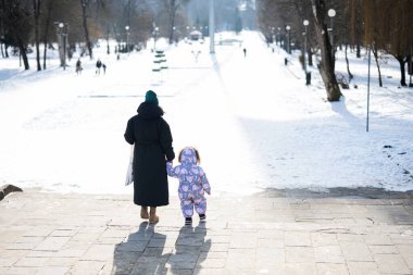 Back view of mother and child walking on a sunny frosty winter day in the park. Mom and daughter.
