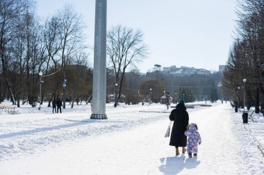 Back view of mother and child walking on a sunny frosty winter day in the park.