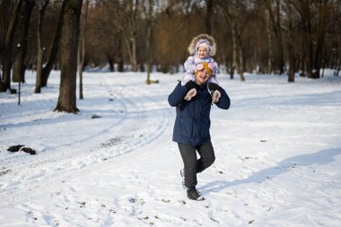 Father hold child on shoulders at sunny frosty winter day in the park. Dad and daughter love.