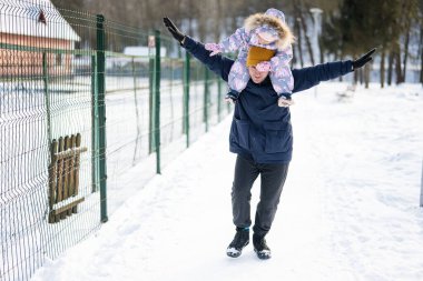 Father hold child on shoulders at sunny frosty winter day in the park. Dad and daughter love.