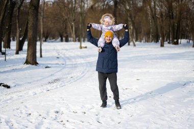 Father hold child on shoulders at sunny frosty winter day in the park. Dad and daughter love.