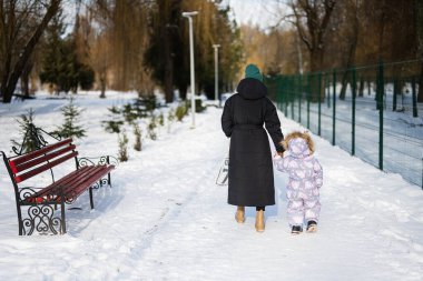 Back view of mother and child walking on a sunny frosty winter day in the park. Mom and daughter.