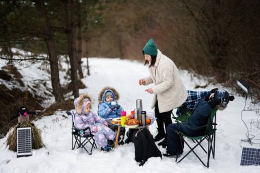 Young woman with children in winter forest on a picnic. Mother and three kids.