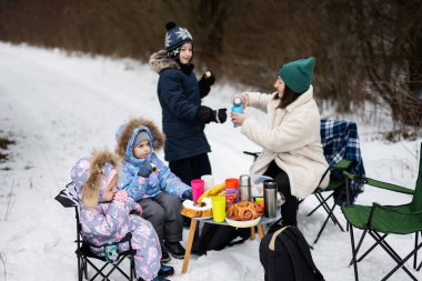 Young woman with children in winter forest on a picnic. Mother and three kids.