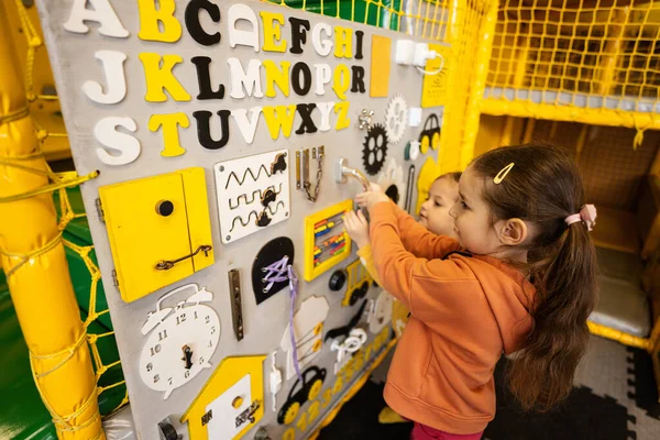 Two sisters playing with busy board at kids play center.
