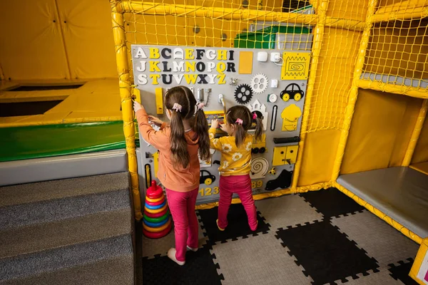 Two sisters playing with busy board at kids play center.