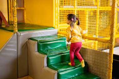 Küçük kız sarı çocuk parkında merdivenlerden çıktı. Etkin eğlencelere katılan çocuk.