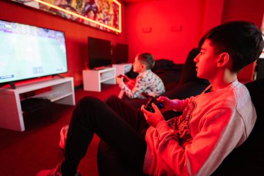 İki erkek oyuncu kırmızı oyun odasında futbol sahası oyun konsolu oynuyorlar..