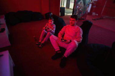 Baba ve oğlu kırmızı oyun odasında oyun konsolu oynuyorlar. Baba ve çocuk oyuncular.