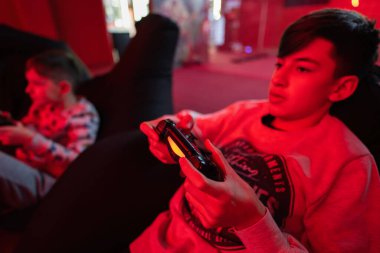 İki erkek oyuncu kırmızı oyun odasında oyun konsolu oynuyorlar..