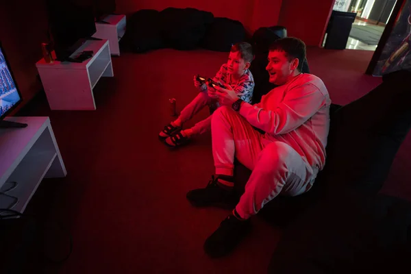 stock image Father and son play gamepad video game console in red gaming room. Dad and kid gamers.