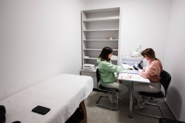 Manikür ustası kadın müşteriyle güzellik salonunda çalışıyor. Manikürcü kadına çivi yaptırıyor..