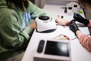 Manikür ustası kadın müşteriyle güzellik salonunda çalışıyor. Manikürcü kadına çivi yaptırıyor..