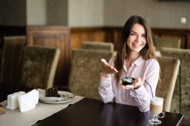 Genç, güzel esmer kadın kafeteryada oturuyor, kapalı bir yerde, çikolatalı kek yiyor, tabağını gösteriyor..