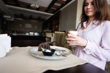 Genç, güzel, esmer bir kadın kafeteryada oturuyor, kapalı bir kafede latte içiyor..